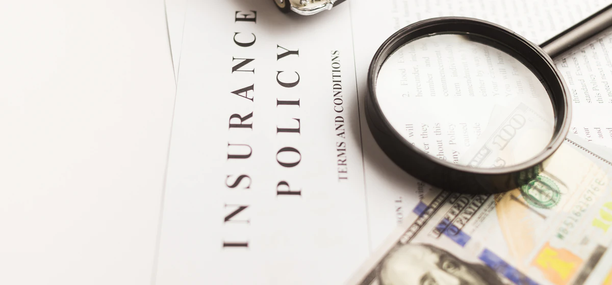 Magnifying glass on an insurance policy beside dollar bills