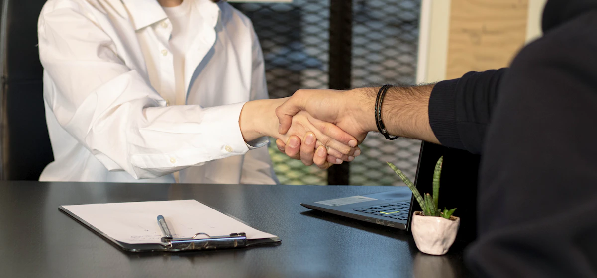 Two people shaking hands across a desk with a clipboard
