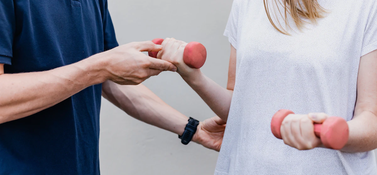 Therapist guiding a patient’s arm during a dumbbell exercise