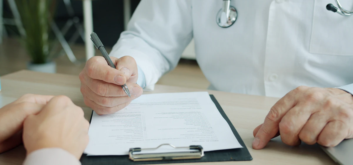 Doctor filling out a form on a clipboard at a desk